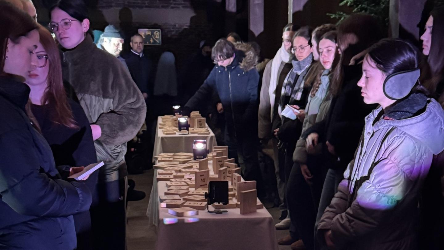 Teilnehmer der Gedenkveranstaltung stehn um Tische mit Holzplättchen zum Gedenken an die einzelnen Deportierten.