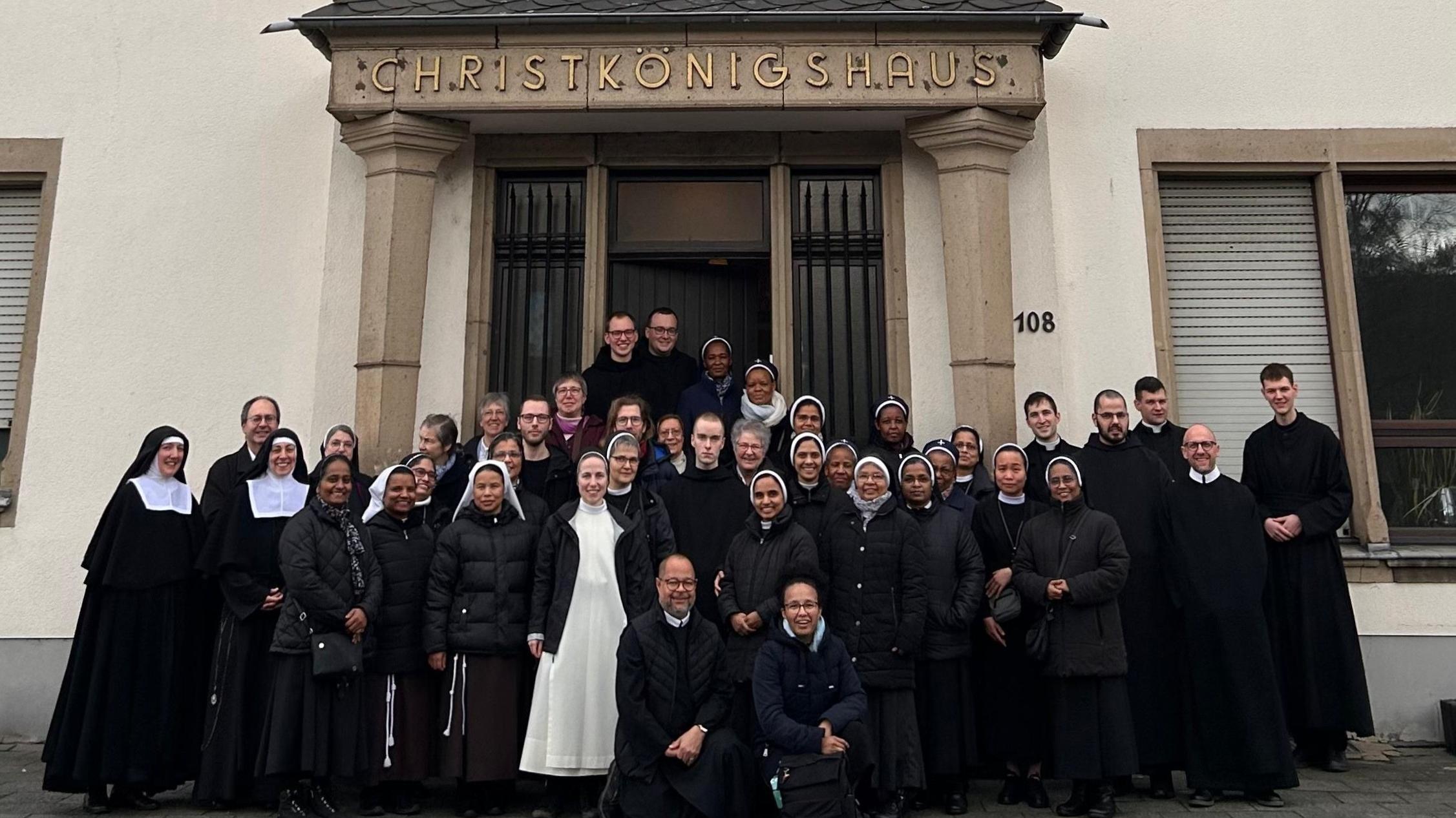 Frauen und Männer mit überwiegend schwarzen Roben stehen vor einer Tür.